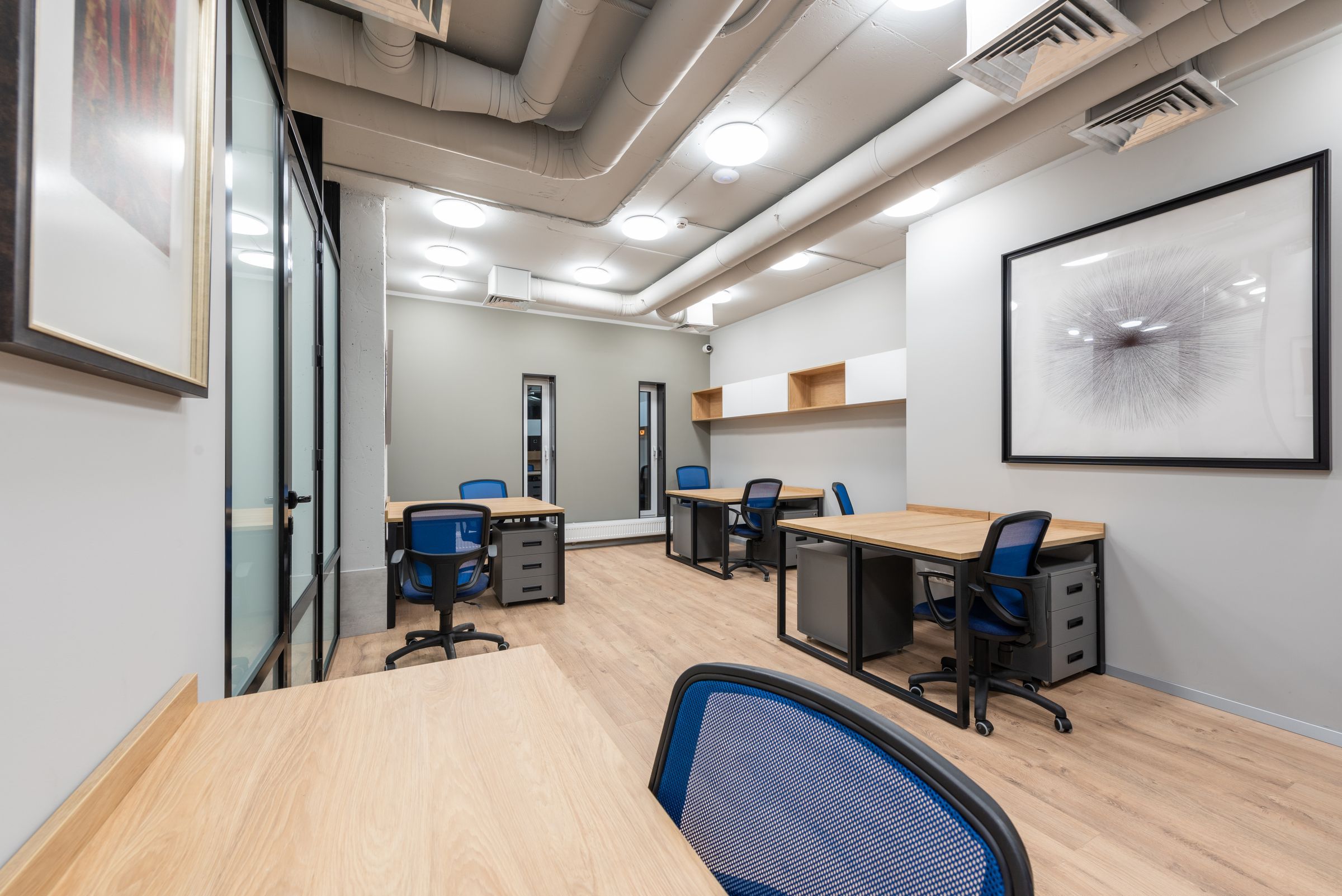 A modern office with light wood desks, blue task chairs and framed artwork