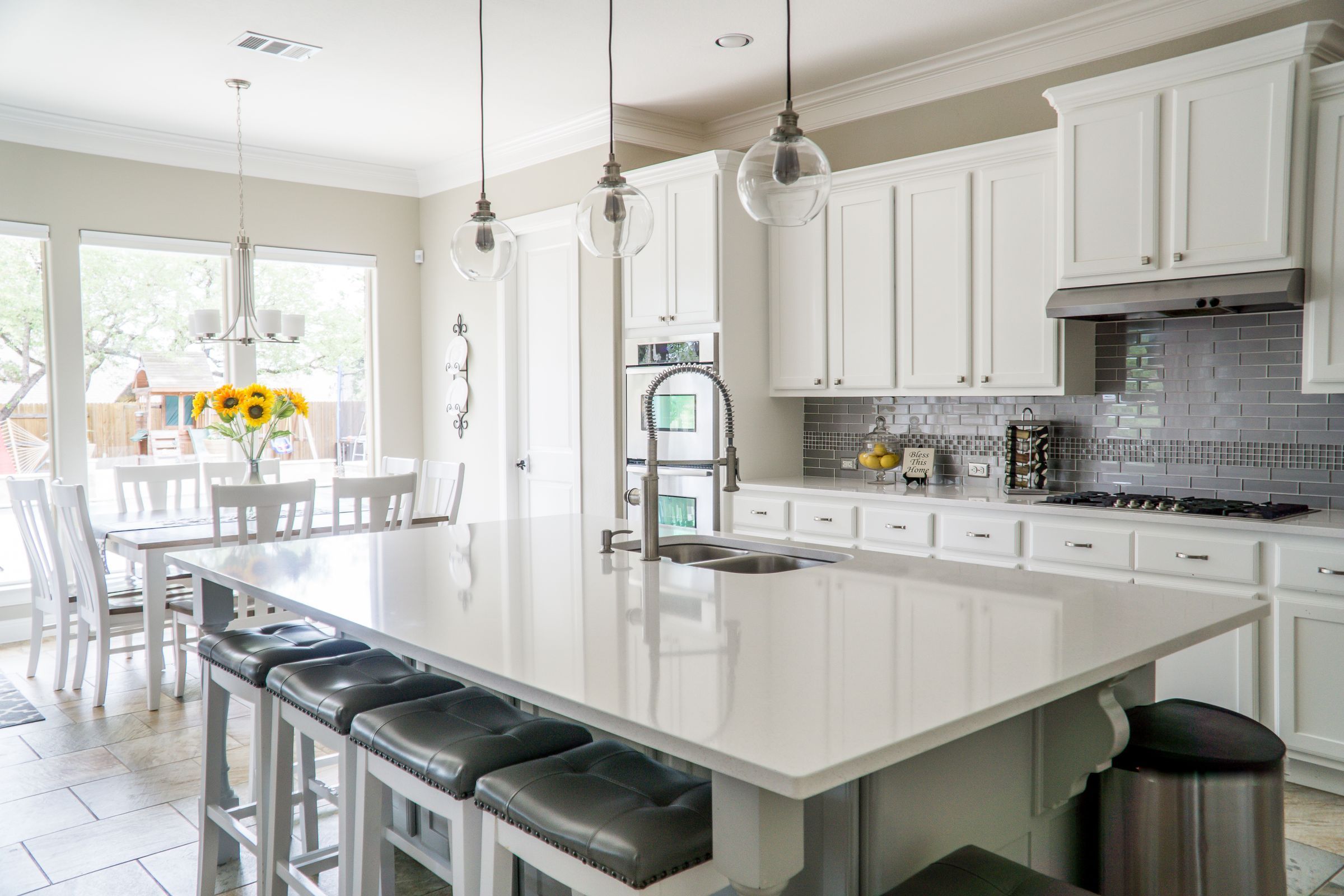 A bright white kitchen with a long quartz island, pendant lights and sunflowers on the dining table
