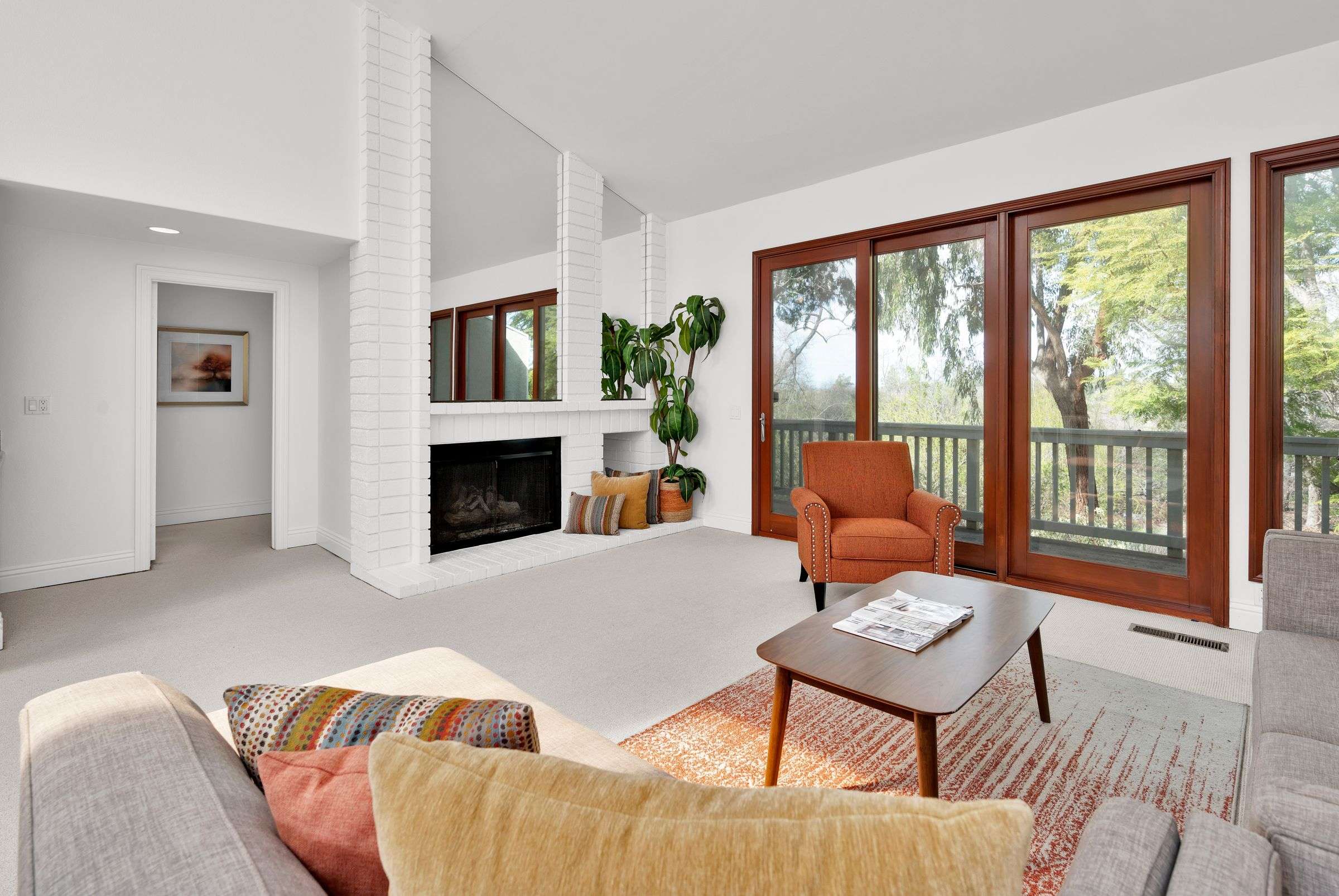 A bright, freshly cleaned living room with a white brick fireplace, tall wood-framed windows and an orange armchair